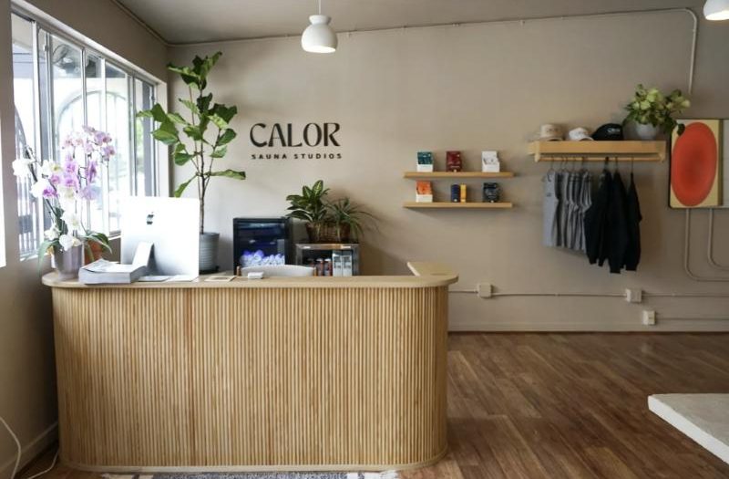Calor's front desk with a slatted wood counter, plants and the Calor sign
